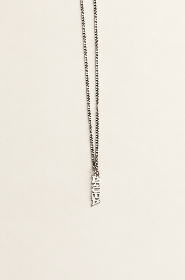 A silver-toned chain necklace with a small vertical pendant spelling 'ARUBA', photographed against a plain off-white background.